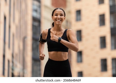 Urban Sports Concept. Young Athletic Female Jogging Outdoors On City Street, Sporty Millennial Woman Wearing Stylish Sportswear, Smartwatch And Armband Running Outside, Enjoying Active Training