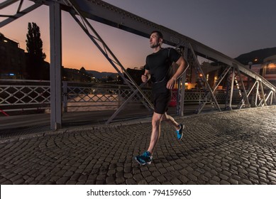 Urban Sports, Young Healthy Man Jogging Across The Bridge In The City At Early Morning In Night