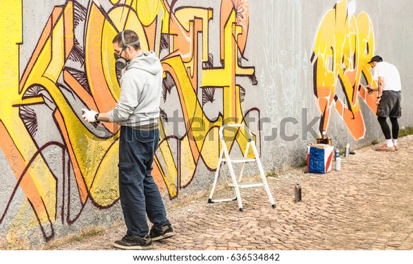 Urban
street artists painting colorful graffiti on generic wall - Modern
art concept with guys performing live murales with aerosol color
spray - Focus on left person - Warm neutral
filter