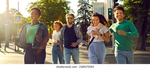 Urban Street Life. Cheerful Group Of Multiracial Friends Walking Around City Running Across Road At Green Traffic Light. Happy Millennial People In Casual Clothes Walk Together On Warm Summer