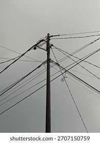Urban Tangle: Low-Angle View of a Rusty Utility Pole with Complex Overlapping Power Lines Against a Gloomy Overcast Sky