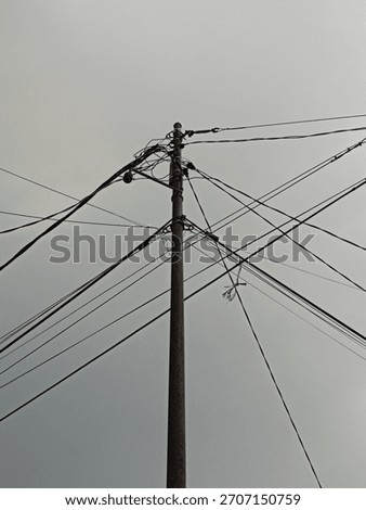Urban Tangle: Low-Angle View of a Rusty Utility Pole with Complex Overlapping Power Lines Against a Gloomy Overcast Sky