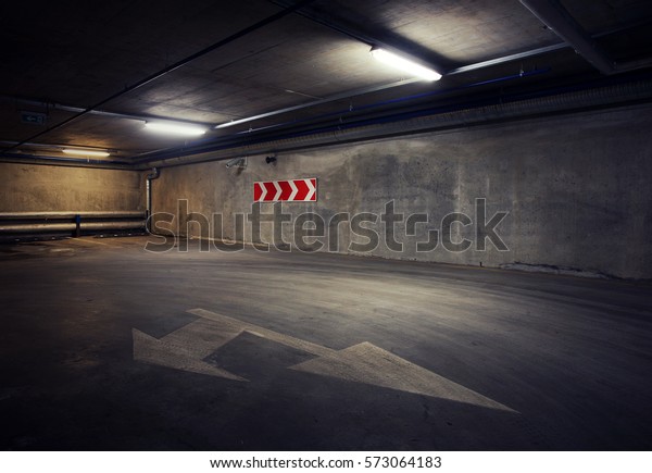 Urban underground\
background. Concrete wall under the lamp light in the dark with\
white arrow on the\
ground.
