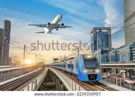 Urban view of railway tracks and suburban electric trains rushing along among high rise buildings. Passenger plane flying in sky, landing at airport. Concept of modern infrastructure transport travel