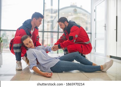 Urgent aid. Male medical workers in red uniform making an injection to a faint woman - Shutterstock ID 1865970214