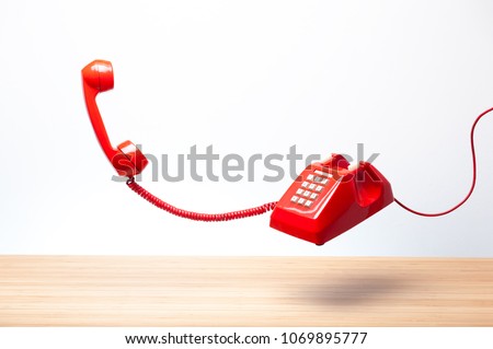Urgent call waiting , classic red telephone receiver, old telephone on white background, flying in weightlessness with wooden desktop.