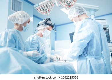 Urgent surgery. Professional smart intelligent surgeons standing near the patient and performing an operation while saving his life - Powered by Shutterstock