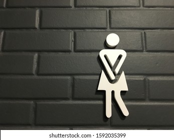 Urinary Urgency Toilet Sign for women at the entrance to a public toilet. Comic toilet sign symbols with woman on black brick background. Copy space. - Shutterstock ID 1592035399