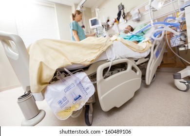 Urine bag attached to bed with nurse and patient in background at hospital