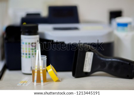 Urine strip and urine cup over urine strip reader in background. concept for laboratory testing 