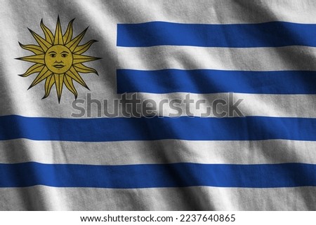 Uruguay flag with big folds waving close up under the studio light indoors. The official symbols and colors in fabric banner