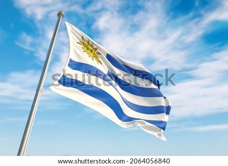 Uruguay flag waving in the wind on flagpole. Perspective wiev Uruguay flag waving a blue cloudy sky
