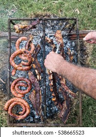 Uruguayan Barbecue On A Grill. Man Cutting Roast Beef At The Countryside