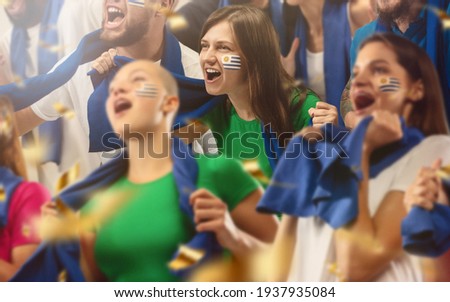 Uruguayan football, soccer fans cheering their team with a blue scarfs at stadium. Excited fans cheering a goal, supporting favourite players. Concept of sport, human emotions, entertainment.