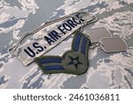 US AIR FORCE branch tape and Airman First Class rank patch and dog tags on digital tiger-stripe pattern Airman Battle Uniform background