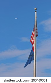 US American And Bergen County, NJ Flags Waving In The Wind With A Jet Plane And The Beautiful Blue Sky In Background.