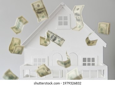 US American Dollar Federal Reserve Bank Notes Cash Flow Falling Over Against A White Model House. Endless Throwing House Money Pit Real Estate Property Inflation Concept.  No People. Copy Space