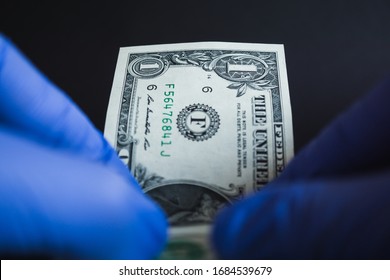 US American One Dollar Banknote Or Bill And Hands With Protective Gloves. Conoravirus Of Covid-19 Pandemic And Its Impact To US Economy, Financial Crisis, Gdp And Health System. Health System Of USA.