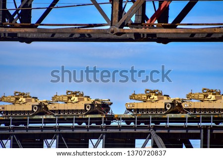 US Army M1 Abrams tanks being transported by railroad over an old trestle bridge.