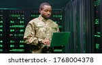 US army male African American officer in uniform stading at server wih secret data and using laptop computer to check the information. Military monitoring service room. Army networking concept.