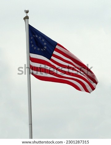 A US Betsy Ross flag flying against overcast skies.