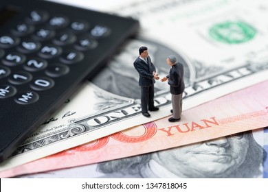 US And China Finance Economic Direction, Trade War, Import And Export Deal And Agreement Concept, Calculator With Miniature Leader Hand Shaking On US Dollar And China Yuan Banknote.