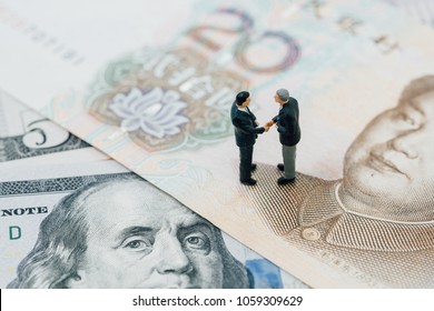 US And China Financial Tariff Trade War Negotiation Talk, Collaboration Or Discuss Concept, Miniature People Businessman Leader Handshaking On Chinese Yuan Banknotes And US Dollar.