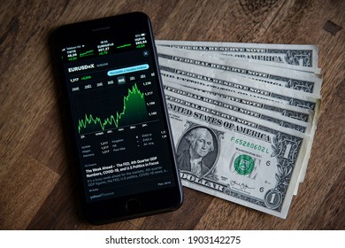 US Dollar Vs Euro Market Exchange Rate On Smart Phone Screen, Trading Table Banknote Graph Analysis. Stock Charts. Paper Money Scattered On A Brown Wooden Table. Budapest, HUNGARY - January 20, 2021