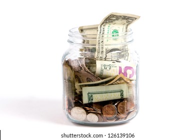 US dollars and coins fill a glass tip jar with money.
