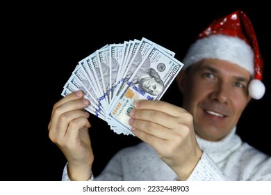 US dollars in hand of happy man in Santa hat on black background. Bonus gift for Christmas celebration, winning lottery at New Year holiday