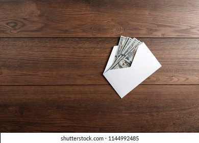 US Dollars In A White Envelope On A Wooden Table. The Concept Of Income, Bonuses Or Bribes. Corruption, Salary, Bonus.