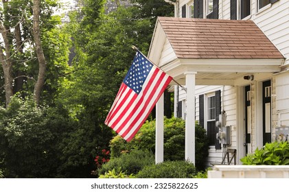 US flag waves proudly in front of an American home, representing the meaning and symbolism of patriotism, American holidays like July 4th and Memorial Day, and the pride of being an American - Powered by Shutterstock