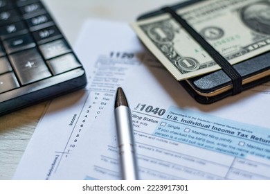 U.S. Individual And Corporation Income Tax Return Close-up Next To A Calculator, Dollars, Money, A Pen And A Notepad On A Wooden Table.