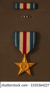 A US Military Silver Star With Ribbon Mounted Against A Plain Brown Background