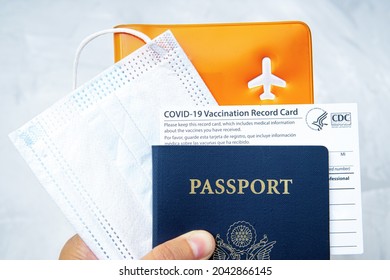 US Passport With A Covid-19 Vaccination Record Card, Face Mask And Documents Organizer In Hand. Pandemic Time Travel Concept.