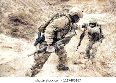 US Ranger, Modern Infantryman, Special Reconnaissance Team Member Or Military Scout In Ammunition, Armed With Service Rifle Helping Brother In Arms To Climb On Sand Dune. Army Brotherhood And Teamwork