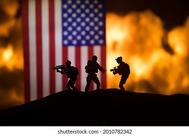 US small flag on burning dark background. Concept of crisis of war and political conflicts between nations. Silhouette of armed soldier against a USA flag. Selective focus