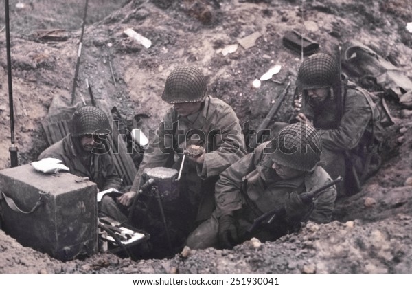 U.S. soldiers of a shore fire control group\
operating Signal Corps radios. One man cranks the hand generator,\
while another uses a hand-held radio set. June 6-8, 1944, Normandy,\
France.