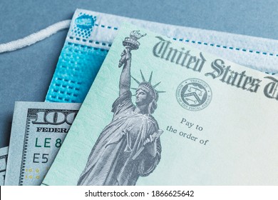 A US stimulus check on with some one-hundred-dollar bills and a medical mask