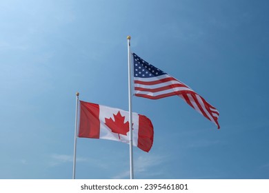 USA and Canadian flags waving left to right against blue sky. Economy, politics concept. - Shutterstock ID 2395461801