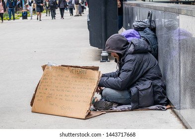 USA, Chicago, Illinois. May 9, 2019. Homeless veteran sitting on the roadside holding a cardboard sign, asking for help, downtown