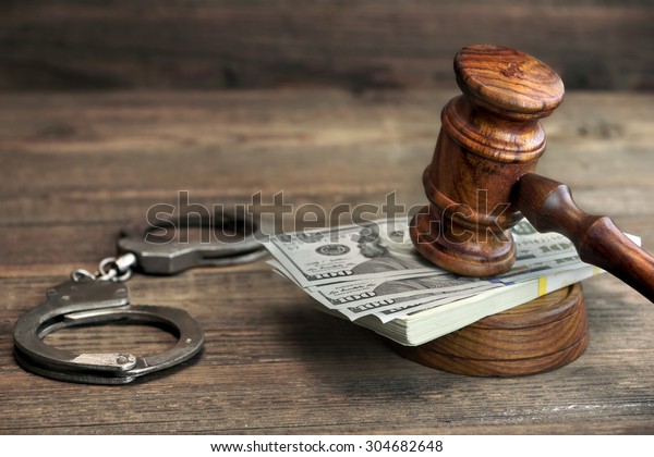 USA Dollar Money Cash, Real Handcuffs And Judge\
Gavel On Rough Wood Background. Concept For Arrest, Corruption,\
Bail, Crime, Bribing or\
Fraud.