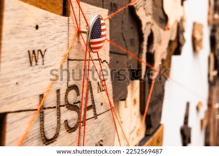 USA flag on the pushpin with red thread showed the paths of movement or areas of influence in the global economy on the wooden map. Planning of traveling or logistic concept. Network connection. 