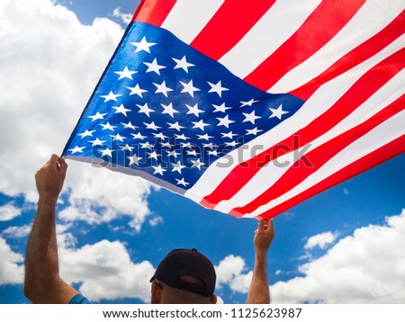 USA Independence day, 4 July. Close up Man hand holding United State of America flag on the blue sky background.