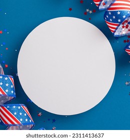 USA's Independence Day theme depicted. Square top view of iconic party embellishments, curly ribbons with American flag pattern, glistening confetti, blue background with an empty circle for text - Shutterstock ID 2311413637