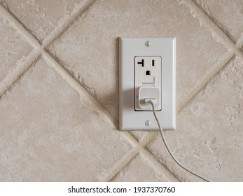 USB cell phone power adapter brick and cord in GFCI wall plug. Electrical cord and charger plug in wall outlet.