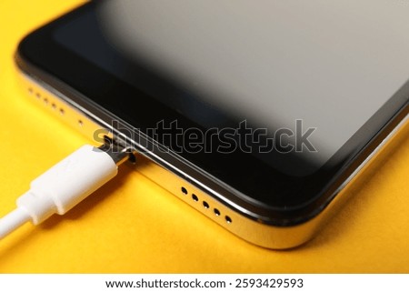 USB charge cable connected to smartphone on orange background, closeup
