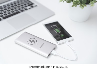 USB Charger Plugged In To Smart Phone. Power Bank, Mobile Phone Battery On Desk Concept