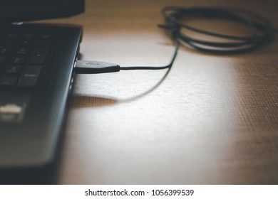 USB Chord Connected With A Laptop Kept On A Wooden Office Table.