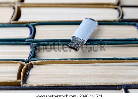 USB flash card on the background of a large stack of old shabby books. Portability of modern information storage media.